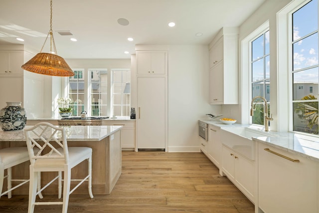 kitchen featuring a kitchen breakfast bar, white cabinets, light wood-type flooring, and a healthy amount of sunlight