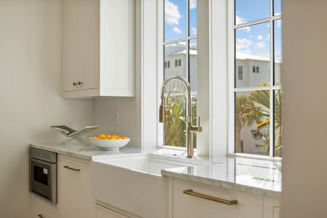 interior space with sink, white cabinetry, and light stone counters