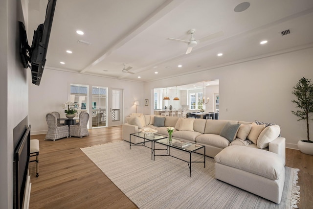 living room featuring ceiling fan, crown molding, beam ceiling, and light wood-type flooring