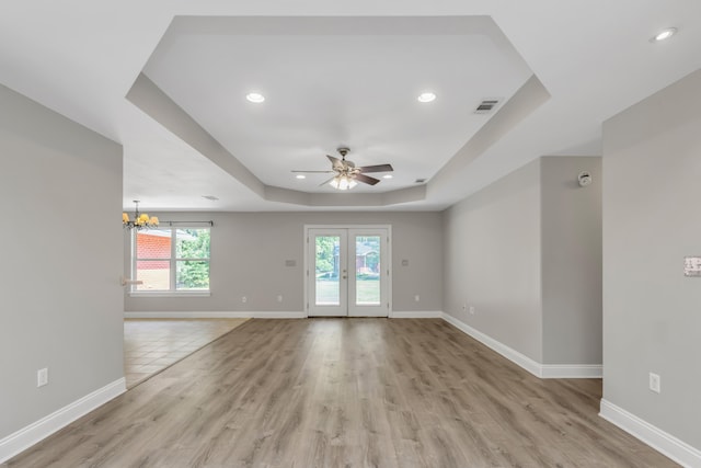 empty room featuring french doors, ceiling fan with notable chandelier, light hardwood / wood-style flooring, and a raised ceiling