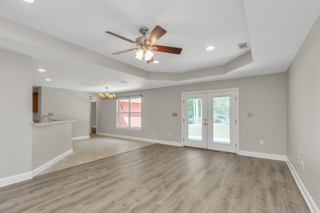 unfurnished room with sink, french doors, a raised ceiling, ceiling fan with notable chandelier, and light wood-type flooring