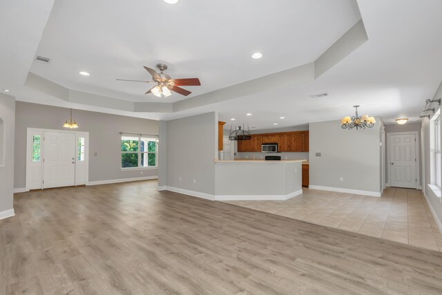 unfurnished living room featuring ceiling fan with notable chandelier, light hardwood / wood-style floors, and a tray ceiling