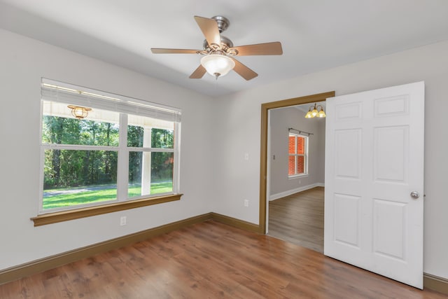 empty room with ceiling fan with notable chandelier and wood-type flooring