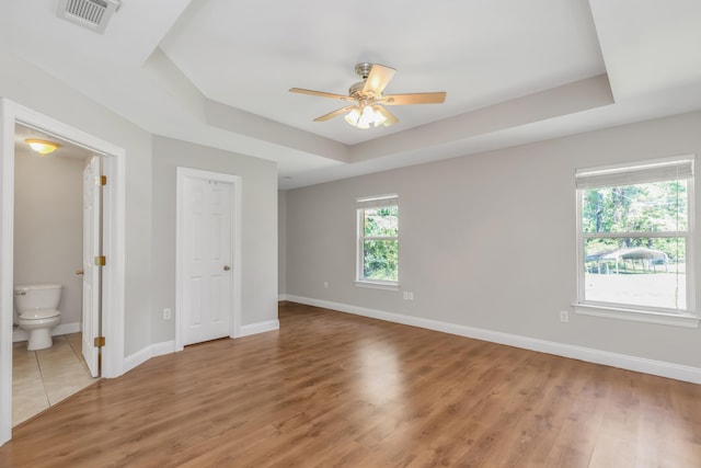 interior space featuring ensuite bathroom, a raised ceiling, ceiling fan, wood-type flooring, and a closet