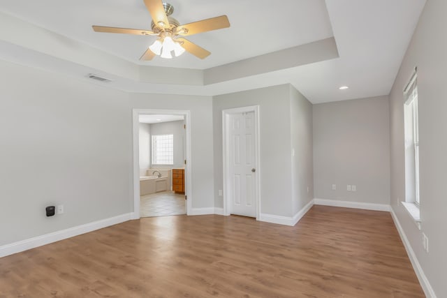 empty room with light wood-type flooring, a raised ceiling, and ceiling fan