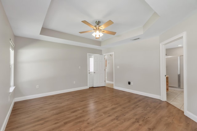 empty room featuring a raised ceiling, ceiling fan, and wood-type flooring