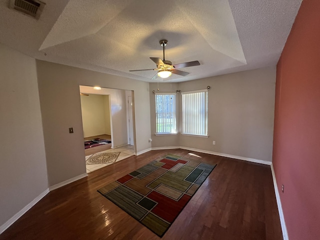 unfurnished room with a textured ceiling, visible vents, wood finished floors, and a ceiling fan
