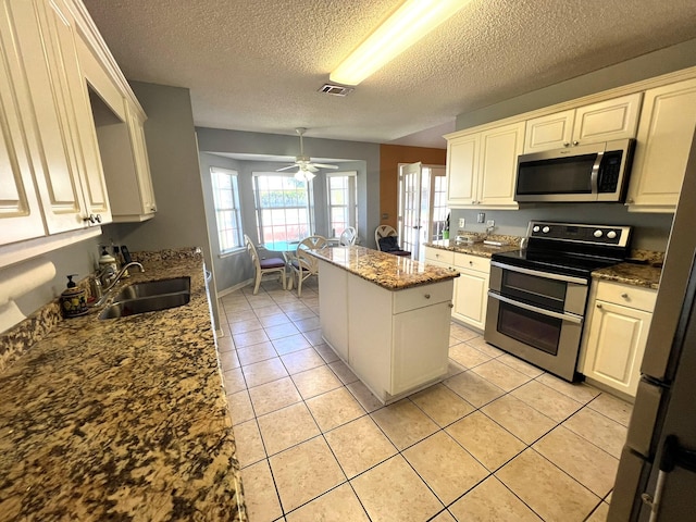 kitchen with sink, a textured ceiling, dark stone counters, a kitchen island, and stainless steel appliances