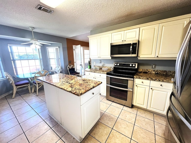 kitchen featuring visible vents, ceiling fan, stone counters, a kitchen island, and appliances with stainless steel finishes