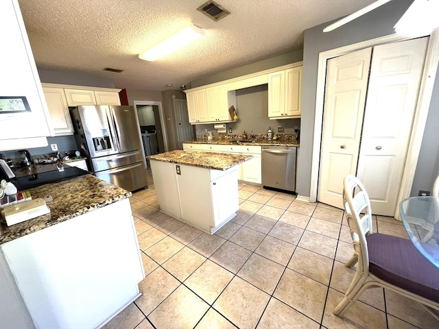kitchen featuring a center island, dark stone countertops, a textured ceiling, visible vents, and appliances with stainless steel finishes