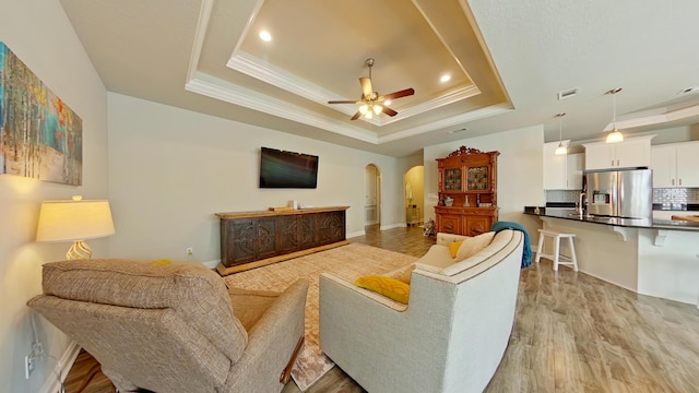 living room with ceiling fan, light hardwood / wood-style floors, a raised ceiling, sink, and ornamental molding