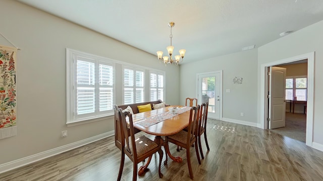 dining room featuring a healthy amount of sunlight, wood-type flooring, and an inviting chandelier