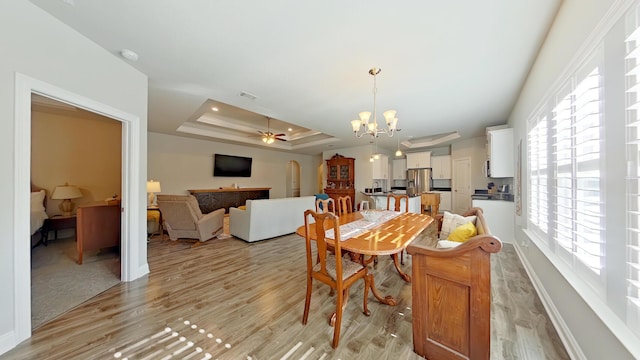 dining space featuring light hardwood / wood-style floors, a tray ceiling, and ceiling fan with notable chandelier