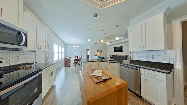 kitchen with white cabinets, decorative light fixtures, butcher block counters, stainless steel appliances, and kitchen peninsula