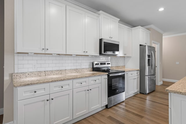 kitchen with white cabinetry, ornamental molding, stainless steel appliances, and light wood-type flooring