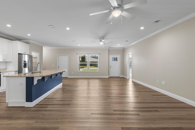 kitchen with a breakfast bar, white cabinets, an island with sink, and stainless steel refrigerator with ice dispenser