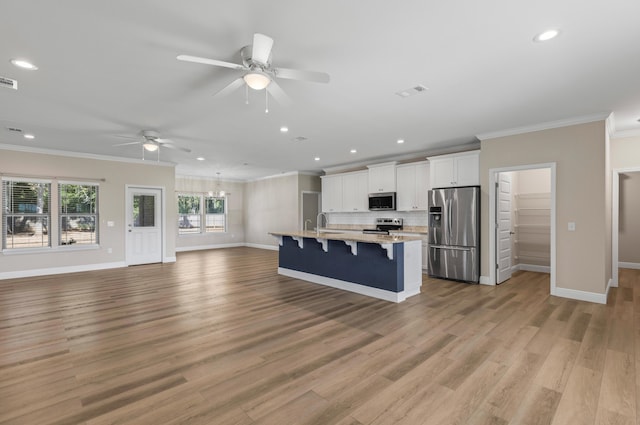 kitchen with backsplash, a kitchen island with sink, white cabinets, appliances with stainless steel finishes, and a kitchen bar