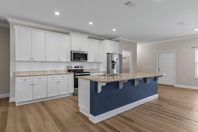 kitchen with a kitchen bar, white cabinetry, a kitchen island with sink, and appliances with stainless steel finishes