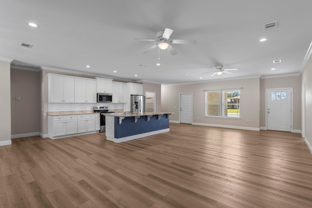 kitchen featuring a breakfast bar, white cabinets, a center island with sink, ceiling fan, and appliances with stainless steel finishes