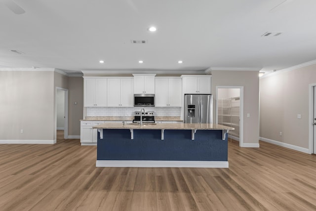 kitchen with appliances with stainless steel finishes, a center island with sink, and white cabinetry