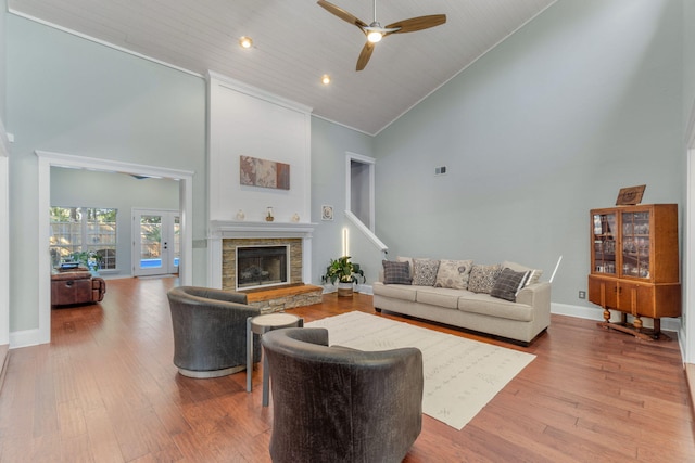 living room featuring ceiling fan, high vaulted ceiling, wooden ceiling, light wood-type flooring, and a stone fireplace