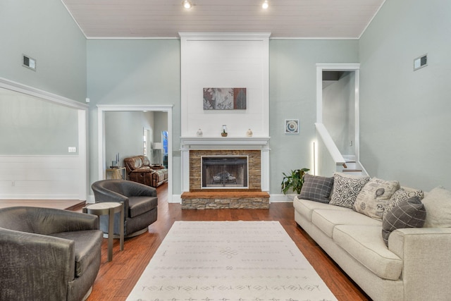 living room featuring crown molding, hardwood / wood-style flooring, a towering ceiling, and a stone fireplace