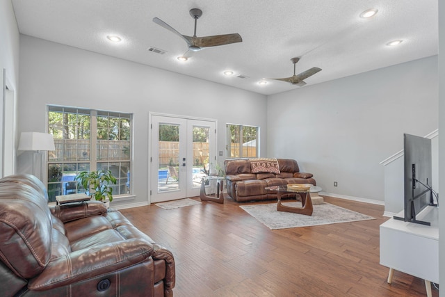 living room with french doors, a high ceiling, wood-type flooring, a textured ceiling, and ceiling fan