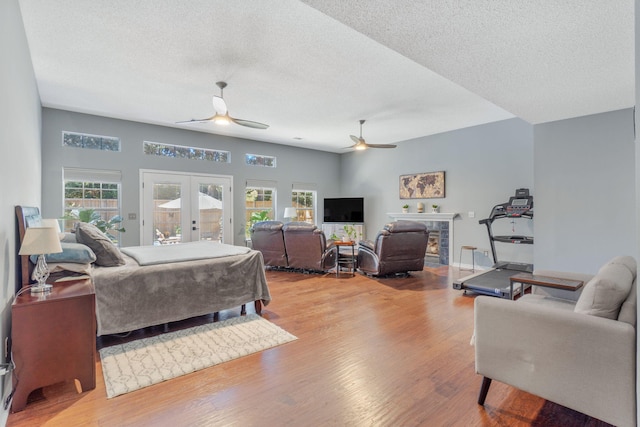 bedroom featuring ceiling fan, access to outside, light wood-type flooring, a stone fireplace, and french doors