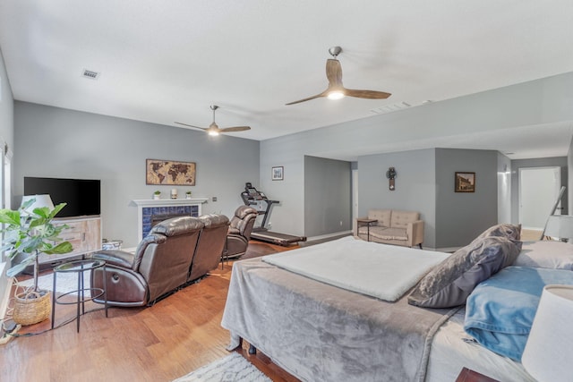 bedroom with a tiled fireplace, hardwood / wood-style flooring, and ceiling fan