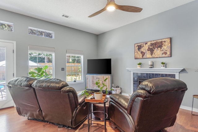 living room with a textured ceiling, a tiled fireplace, hardwood / wood-style flooring, and ceiling fan