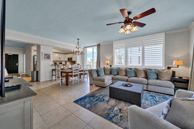 tiled living room with crown molding and ceiling fan with notable chandelier