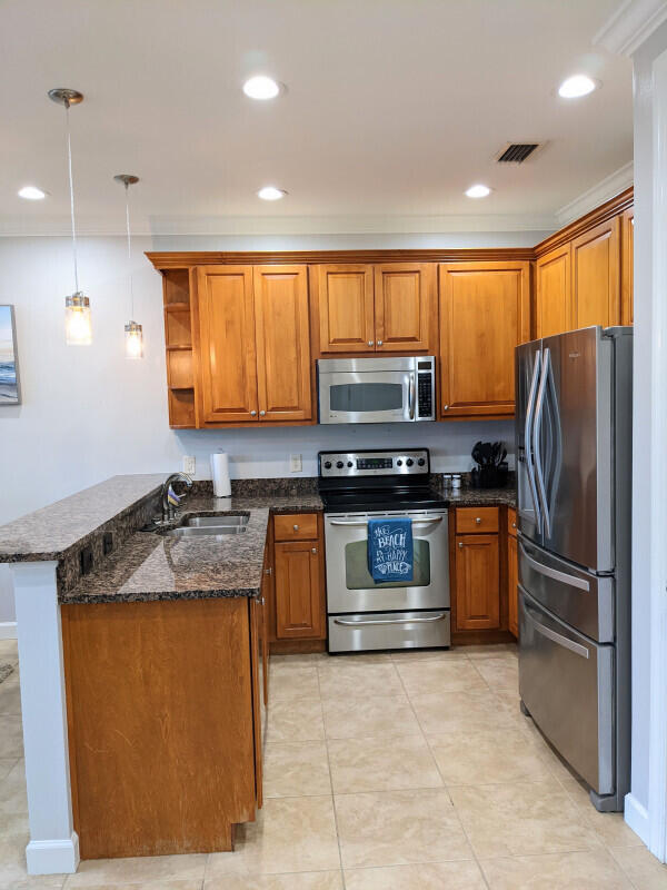 kitchen featuring appliances with stainless steel finishes, sink, kitchen peninsula, dark stone counters, and decorative light fixtures