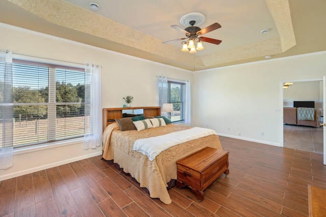 bedroom featuring dark hardwood / wood-style floors, a raised ceiling, multiple windows, and ceiling fan