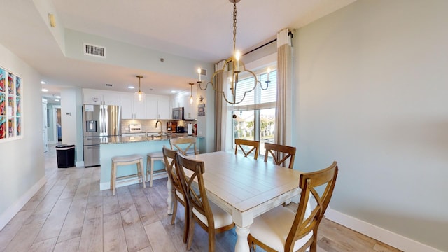 dining room with a chandelier, sink, and light wood-type flooring