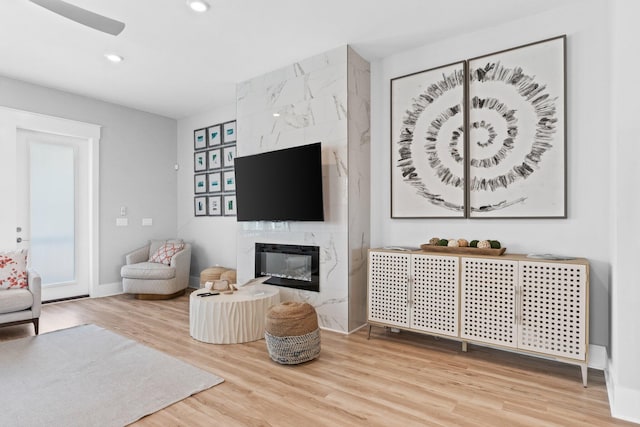 living room with a premium fireplace, wood-type flooring, and ceiling fan