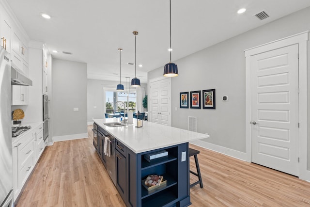 kitchen featuring an island with sink, hanging light fixtures, sink, light wood-type flooring, and white cabinetry