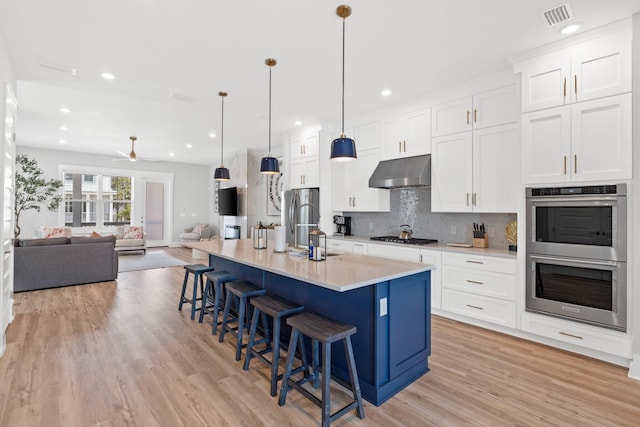 kitchen with a center island with sink, extractor fan, appliances with stainless steel finishes, white cabinetry, and light hardwood / wood-style floors