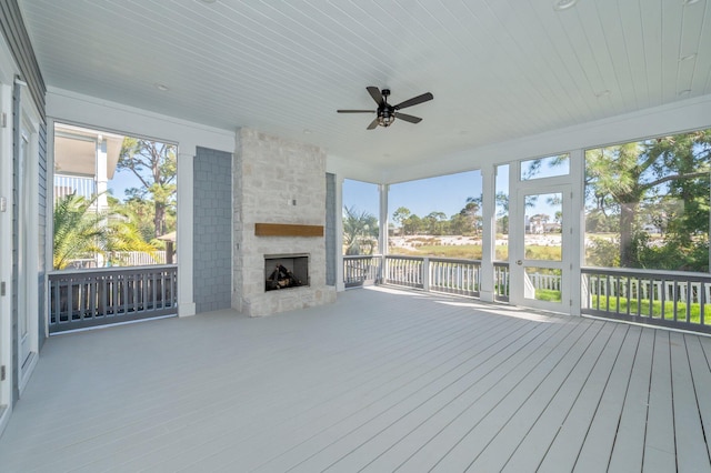 unfurnished sunroom with a stone fireplace and ceiling fan