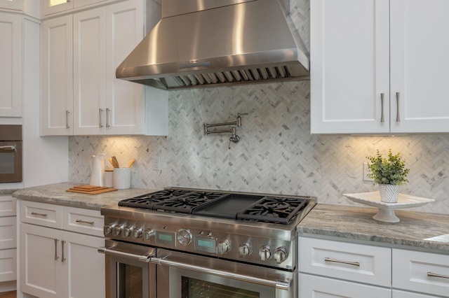 kitchen featuring white cabinets, wall chimney exhaust hood, light stone countertops, and stainless steel appliances