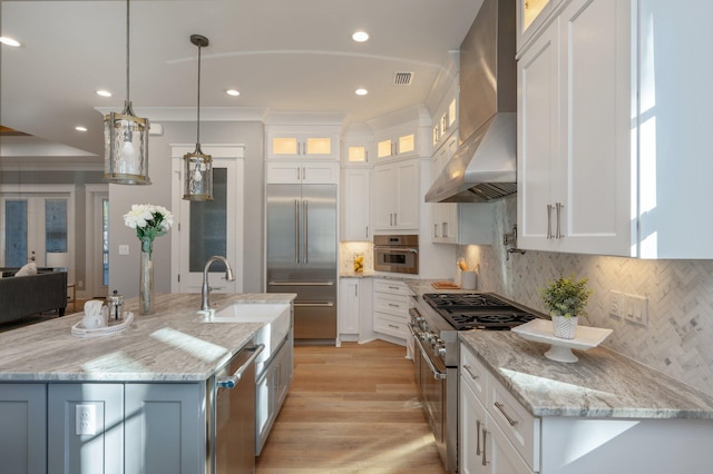 kitchen with white cabinets, wall chimney exhaust hood, decorative light fixtures, and high end appliances