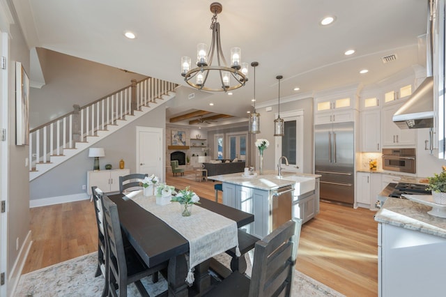 dining space with sink, beamed ceiling, a notable chandelier, and light hardwood / wood-style flooring