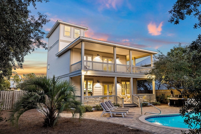 back house at dusk featuring a patio area, a fenced in pool, and a balcony