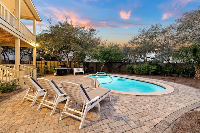 pool at dusk featuring a patio and area for grilling