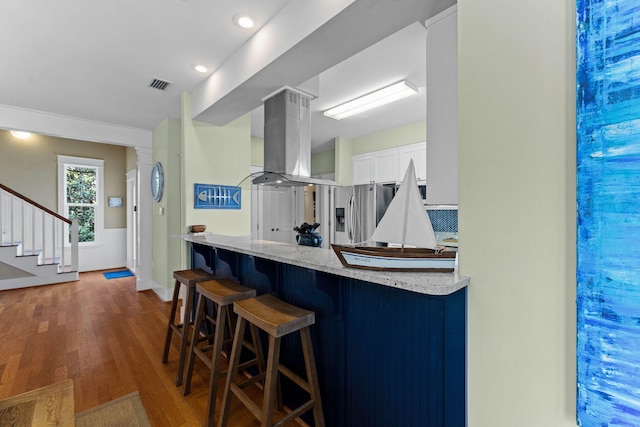 kitchen with island exhaust hood, stainless steel fridge with ice dispenser, a breakfast bar area, white cabinetry, and dark wood-type flooring