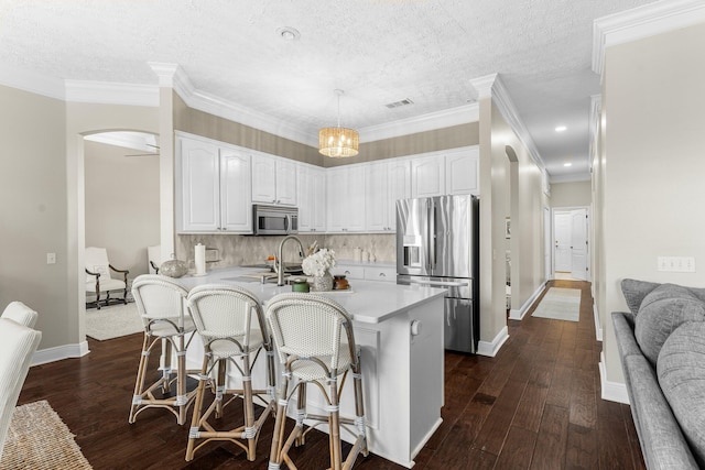 kitchen featuring dark wood-type flooring, a kitchen bar, pendant lighting, white cabinetry, and appliances with stainless steel finishes