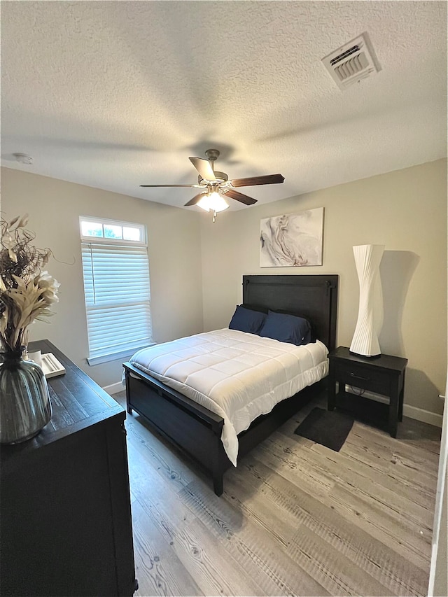 bedroom with light hardwood / wood-style flooring, a textured ceiling, and ceiling fan