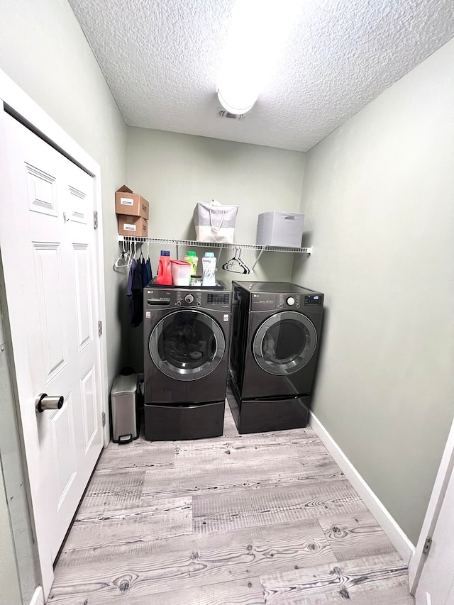 clothes washing area with a textured ceiling, washing machine and dryer, and light hardwood / wood-style flooring