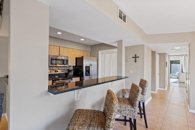 kitchen with kitchen peninsula, backsplash, appliances with stainless steel finishes, a kitchen bar, and dark stone countertops