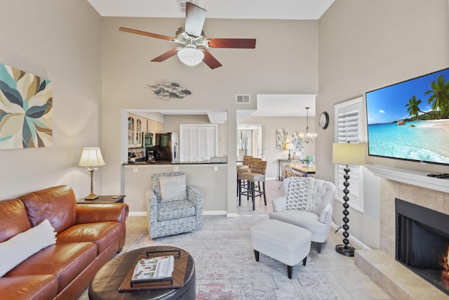 living room with a high ceiling, ceiling fan with notable chandelier, a fireplace, and light tile patterned floors