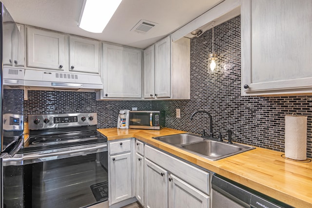 kitchen with decorative backsplash, hanging light fixtures, appliances with stainless steel finishes, sink, and butcher block countertops